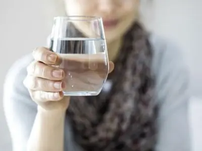 Woman holding a clear glass of water, symbolizing the benefits of water filtration systems for improved water quality and safety.