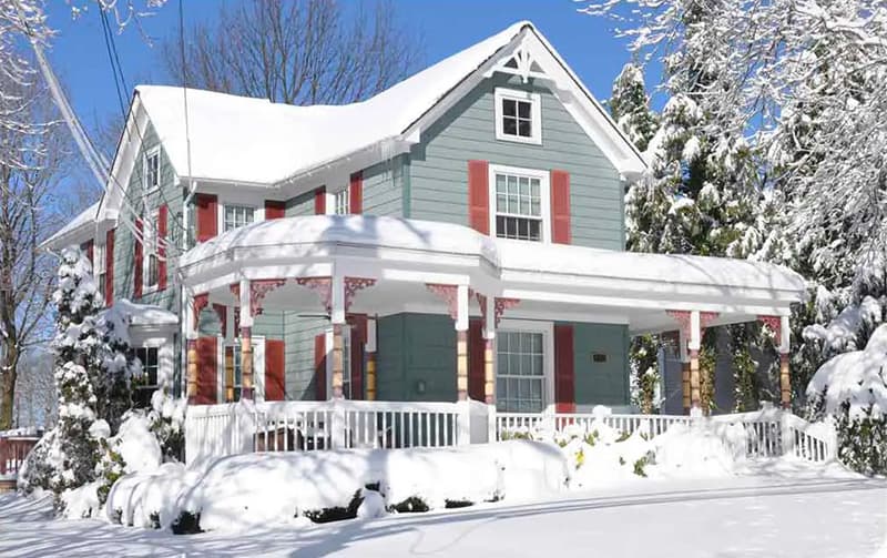 Snow-covered house with a porch in winter, showcasing residential plumbing and HVAC considerations for cold weather maintenance.