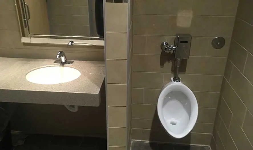 Commercial restroom with a modern sink and urinal, featuring tiled walls and a mirror, showcasing A & W Plumbing's installation work.