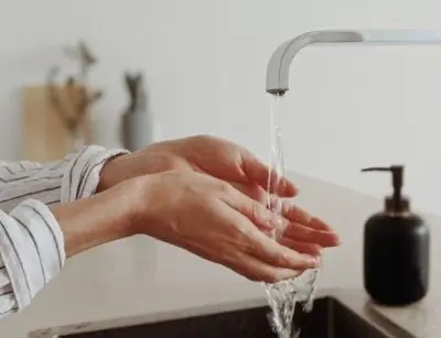 Hands under a modern kitchen faucet with running water, illustrating essential home plumbing and water supply systems.