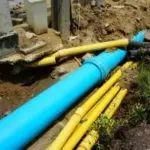 Large blue and yellow pipes on rugged ground, highlighting outdoor plumbing installation by A & W Plumbing and Heating, Inc.