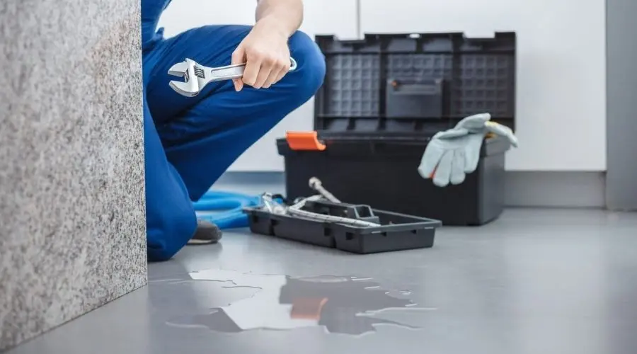 Plumber in blue attire holding a wrench near a toolbox and water puddle, showcasing A & W Plumbing services.