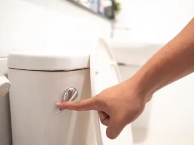 Hand pressing flush button on a toilet, emphasizing proper maintenance and prevention of sewer clogs in plumbing systems.