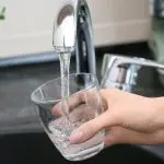 Hand filling a glass with clean water from a kitchen faucet, highlighting the importance of safe water supply and backflow prevention.