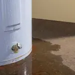 Leaking water heater tank with visible water pooling on the floor, highlighting the need for repair or replacement services from A & W Plumbing and Heating, Inc.