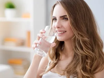 Woman drinking clean water from a glass, emphasizing the importance of safe water supply and backflow prevention.