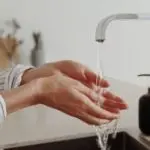 Human hands washing in a modern kitchen sink with soap, highlighting plumbing maintenance and cleanliness essentials.