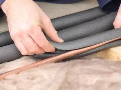 Person installing pipe insulation to prevent frozen and burst pipes during winter.