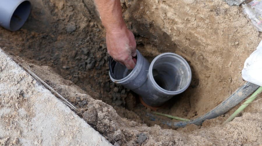 Person installing gray PVC plumbing pipes in a trench, illustrating plumbing repair techniques relevant to toilet maintenance and plumbing services.