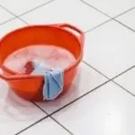 Bright orange cleaning bucket with soapy water and blue cloth on tiled floor, representing cleanliness for plumbing services.