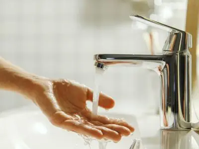 Hand under a modern faucet with water flowing, illustrating the functionality of tankless water heaters in providing on-demand hot water.