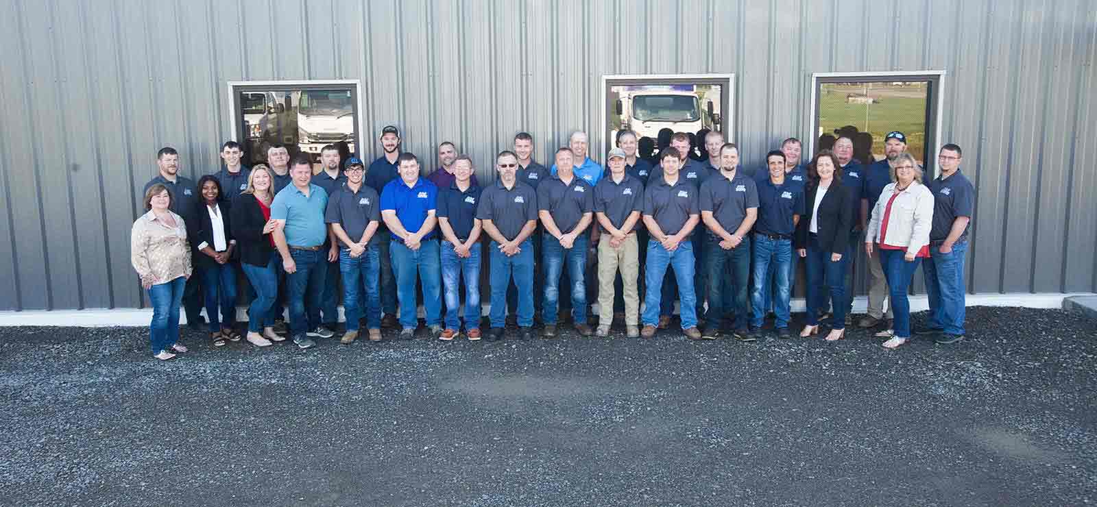 Group photo of A & W Plumbing and Heating, Inc. team standing outside their facility, showcasing a diverse team of plumbers and HVAC technicians in branded shirts, emphasizing community and family-oriented work culture.