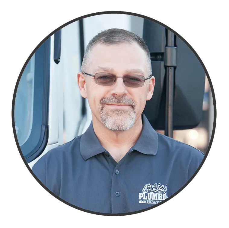 Plumber from A & W Plumbing and Heating, Inc. wearing a branded shirt, smiling in front of a service vehicle, showcasing expertise and friendly service.