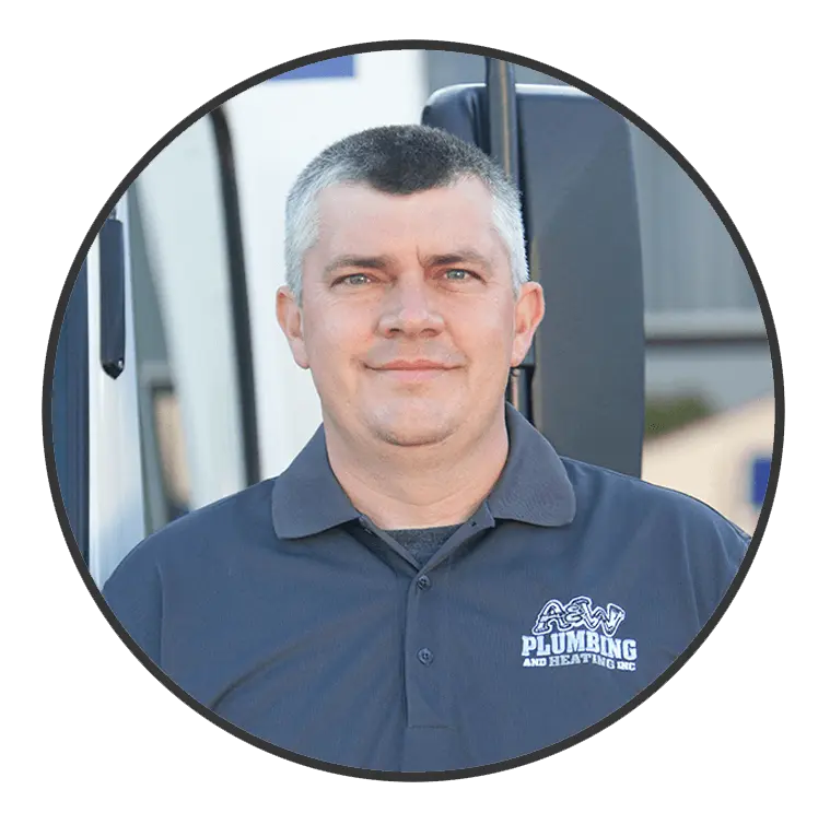 Man in a gray polo shirt with "PLUMBING AND HEATING INC." logo, smiling in front of a service vehicle, representing the A & W Plumbing and Heating, Inc. team.