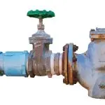 Industrial valve and water meter with green handle and rusted pipe, emphasizing plumbing safety and backflow prevention.