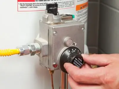 Hand adjusting the thermostat dial on a gas water heater, illustrating common maintenance tasks related to water heater repair and efficiency.