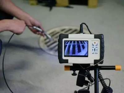 Person using a sewer video inspection camera to diagnose sewer line issues, with a focus on the monitor displaying the inside of the sewer drain.