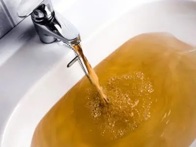 Brown, contaminated water flowing from a faucet into a sink, illustrating the dangers of backflow and potential water contamination.