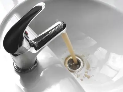 Faucet pouring brown water into sink drain, illustrating potential backflow contamination risks in plumbing systems.