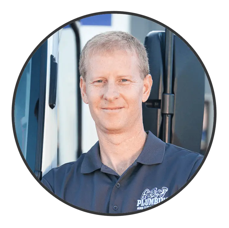 Smiling male plumber in a gray A & W Plumbing and Heating polo shirt, standing near a service vehicle, representing the skilled team at A & W Plumbing and Heating, Inc. in Southern Illinois.