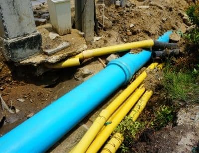 Outdoor plumbing pipes, including blue and yellow drainage pipes, exposed in a dug-up area, illustrating potential clogging issues related to outdoor plumbing maintenance.