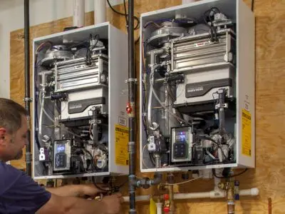Technician installing two tankless water heaters, showcasing their compact design and advanced technology, relevant to efficient home water heating solutions.