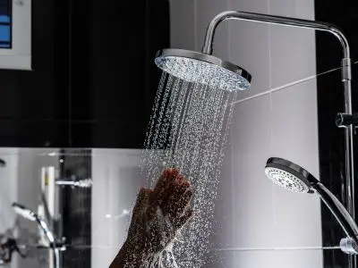 Hand under showerhead with flowing water, illustrating the importance of hot water supply in homes, relevant to water heater repair and maintenance.