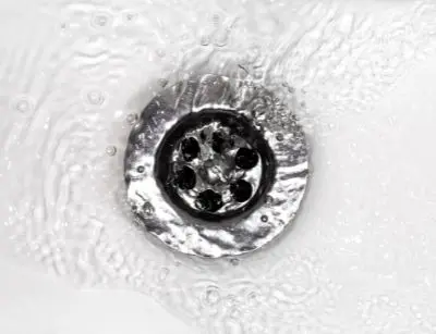 Close-up of a silver sink drain surrounded by flowing water, illustrating the importance of drain maintenance and cleaning in home plumbing systems.
