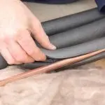 Close-up of a human hand applying gray insulation on a copper pipe for plumbing services by A & W Plumbing and Heating, Inc.