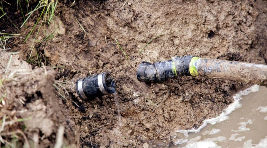 Sewer pipe leaking water in excavated ground, indicating potential plumbing issues and the need for repair or replacement services.