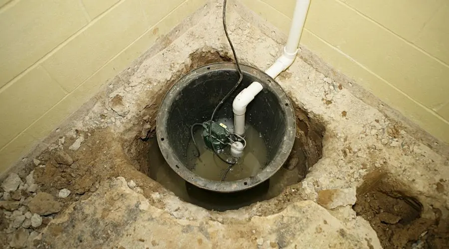 Sump pump installation in a basement sump pit, featuring a metal basin, plastic piping, and water for plumbing solutions.