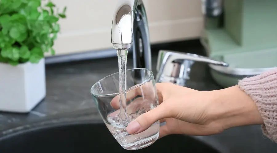 Hand holding a clear glass under a kitchen faucet, filling with water, demonstrating plumbing functionality and water quality.
