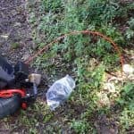 Gardening equipment with orange cord and plastic bag near greenery, representing tools for plumbing and heating maintenance.