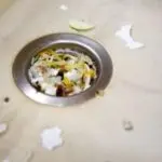 Food remnants around a circular metal drain, highlighting the importance of garbage disposal maintenance for plumbing.