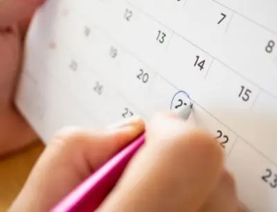 Hand marking a date on a calendar with a pink pen, emphasizing the importance of scheduling regular HVAC maintenance for optimal air conditioning performance.