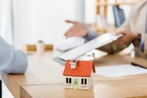 Model house on a table during a consultation about plumbing services, emphasizing home safety and maintenance.