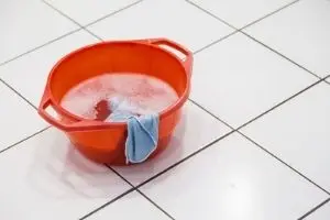 Orange bucket with soapy water and a blue cloth on tiled floor, illustrating cleanup after plumbing backflow issues.