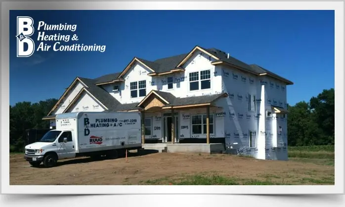 House under construction with B & D Plumbing, Heating & A/C vehicle and visible service branding and construction materials.