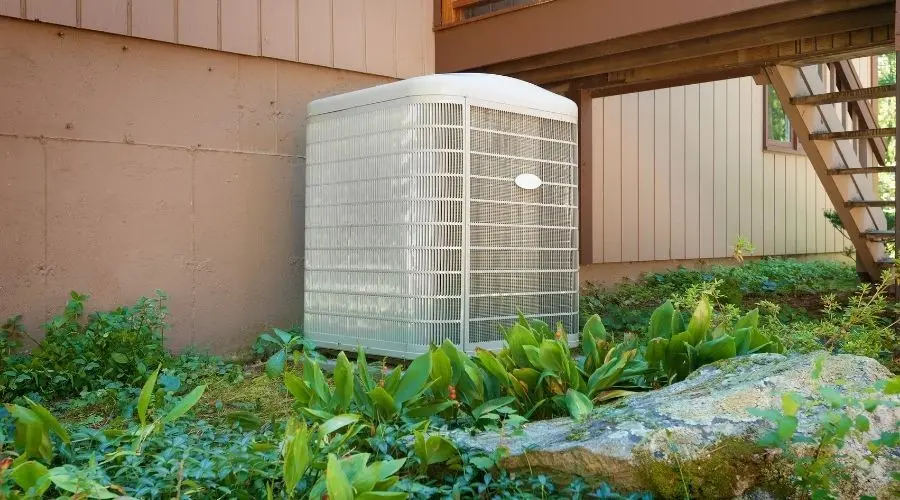 Air conditioning unit in a serene outdoor space with plants and rocks, featuring B & D Plumbing, Heating & A/C.