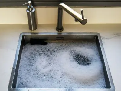 Kitchen sink filled with soapy water, illustrating potential plumbing issues from tree root intrusion affecting sewer lines.