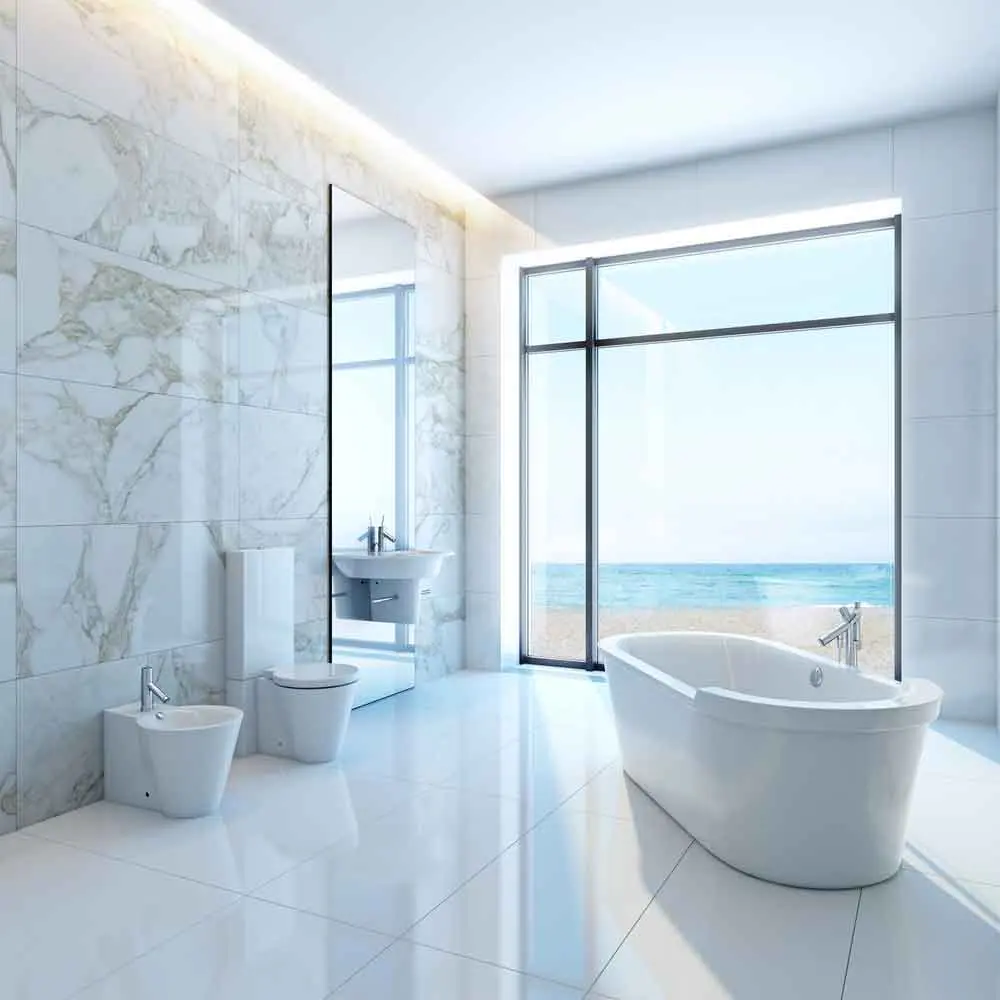 Modern bathroom design featuring a freestanding bathtub, wall-mounted sink, and stylish fixtures, with large windows overlooking a beach view, emphasizing luxury and functionality in bathroom remodeling.