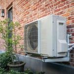 Air conditioning unit on a brick wall near a plant, highlighting B & D Plumbing, Heating & A/C services.