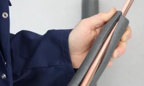 Hand holding insulated copper pipe, demonstrating pipe insulation for preventing freezing during winter plumbing maintenance.