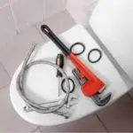 Tools for plumbing repair on a toilet by B & D Plumbing, including an adjustable wrench and hoses.