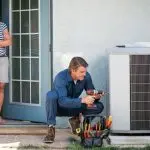 HVAC technician with drill near air conditioning unit, while a woman observes, from Boutwell's Air Masters.