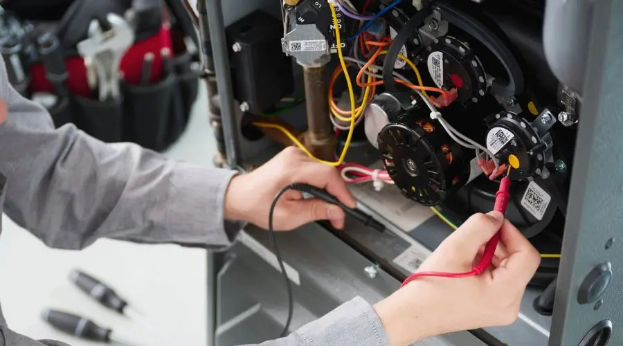 Technician repairing a furnace with tools, showcasing colorful wiring and labeled components in HVAC service work.