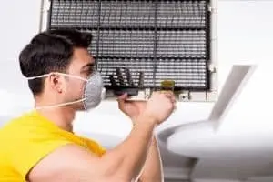 Technician in a mask inspecting HVAC system components, demonstrating maintenance practices for heating and air conditioning systems.
