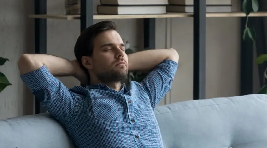 Man relaxing on a couch, eyes closed, in a comfortable indoor setting, representing the comfort and improved air quality provided by UV air sanitizers.