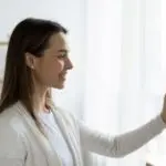Woman engaging with a smartphone in a bright room, highlighting HVAC thermostat settings from Boutwell's Air Masters.