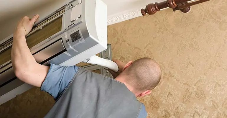 Technician installing ductless mini split air conditioning system on wall, highlighting HVAC service expertise by Boutwell's Air Masters.